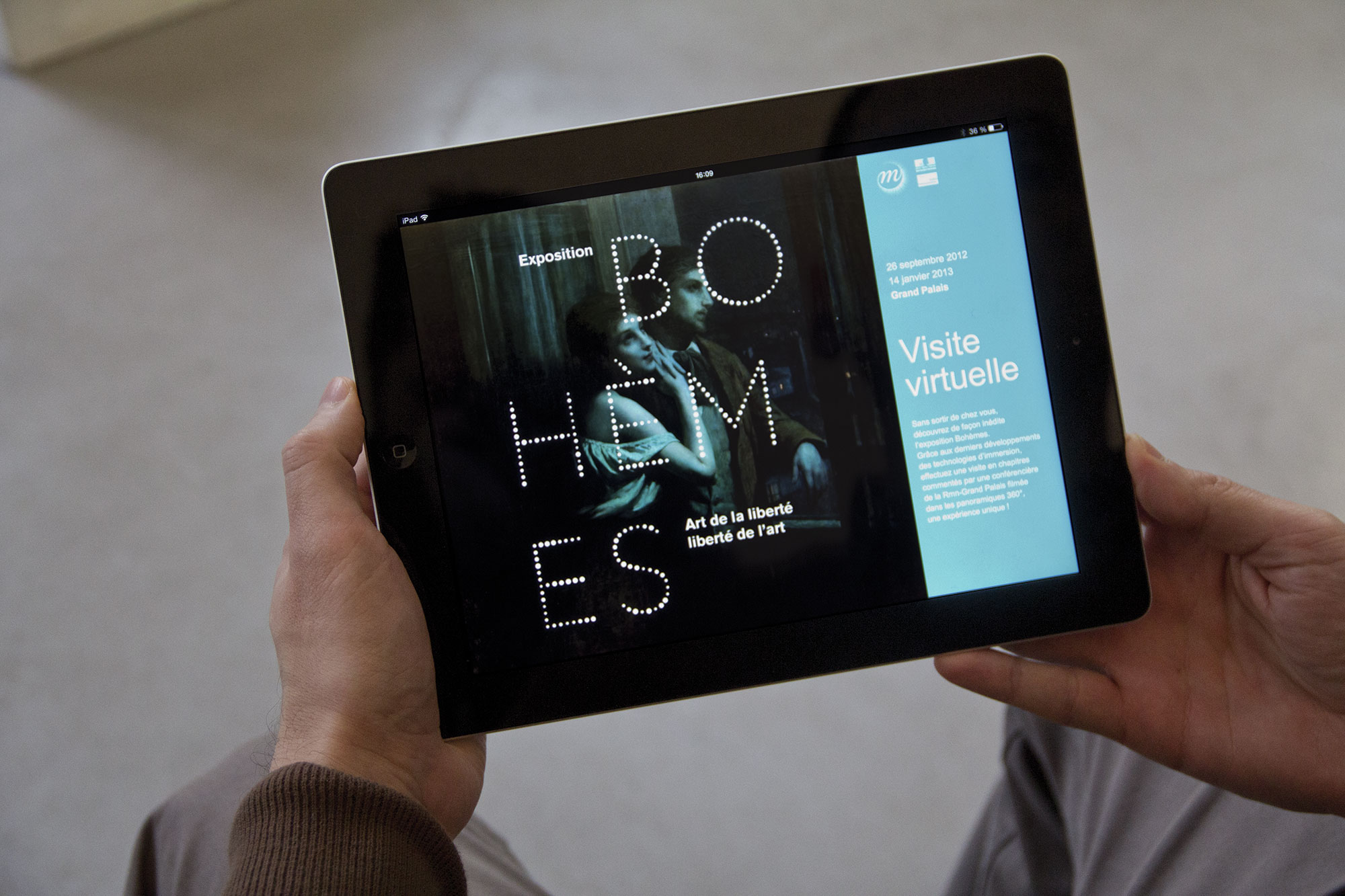 L'image montre une personne tenant une tablette, sur laquelle apparaît une interface d'exposition intitulée "BOHÈMES". L'exposition semble se concentrer sur le thème de l'art et de la liberté. À droite de l'écran, on peut voir des détails sur la visite virtuelle, ainsi qu'une date : 29 septembre 2013. La mise en page est moderne et minimaliste, avec un fond sombre et un texte lumineux.