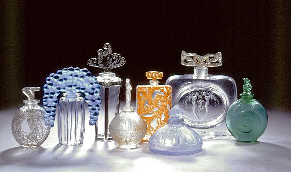 L'image présente une collection de flacons en verre, chacun ayant un design unique et artistique. Les flacons varient en forme et en couleur, allant de transparents à colorés, avec des détails fins et des courbes élégantes. Certains flacons ont des bouchons sculptés, ajoutant à leur esthétique raffinée. L'arrangement met en valeur la diversité des formes et des motifs, créant un effet visuel attrayant. L'éclairage met en avant les textures et les reflets du verre, renforçant leur élégance.