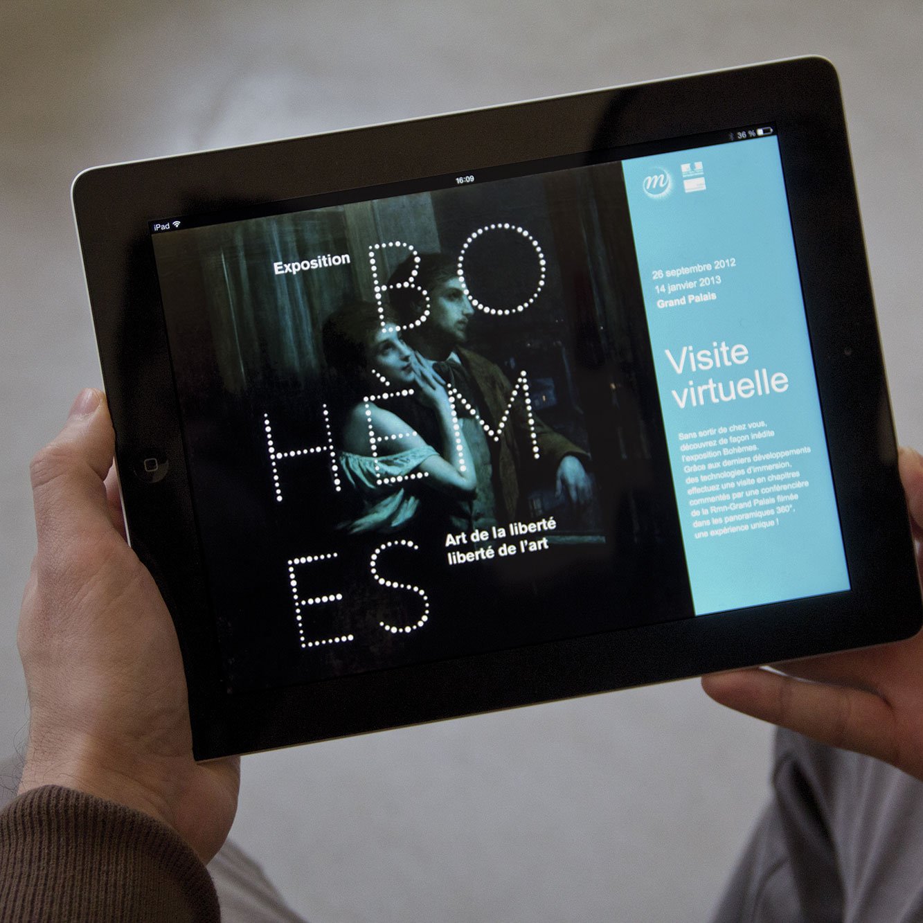 L'image montre une personne tenant une tablette, sur laquelle apparaît une interface d'exposition intitulée "BOHÈMES". L'exposition semble se concentrer sur le thème de l'art et de la liberté. À droite de l'écran, on peut voir des détails sur la visite virtuelle, ainsi qu'une date : 29 septembre 2013. La mise en page est moderne et minimaliste, avec un fond sombre et un texte lumineux.