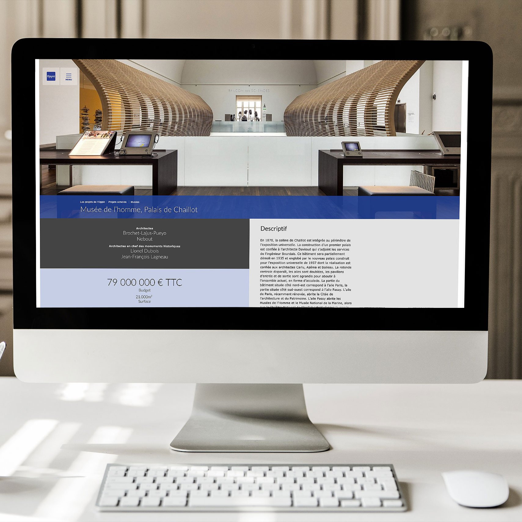 L'image montre un ordinateur de bureau affichant une interface web. L'écran présente un site avec un design moderne, mettant en avant un projet immobilier ou architectural, avec une grande section de texte et des informations financières. On peut apercevoir une table ou un comptoir à l'intérieur d'un espace bien éclairé, probablement un bureau ou une salle d'exposition. Sur le bureau, il y a également une tasse ou un récipient, ce qui ajoute une touche de convivialité à l'environnement de travail.