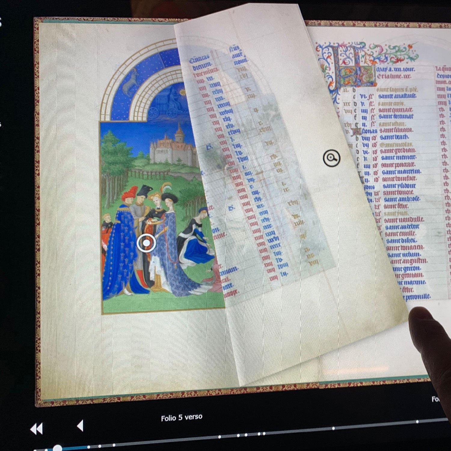 L'image montre une page d'un manuscrit ancien, probablement un livre d'heures ou un autre type de recueil médiéval. À gauche, on peut apercevoir une illustration colorée représentant des figures humaines vêtues de costumes d'époque, se tenant devant un paysage avec un château. À droite, une colonne de texte est visible, répertoriant probablement des noms ou des prières, accompagnée d'une décoration élaborée en haut. Un doigt pointe vers la page, suggérant une interaction avec le contenu. Le fond est sobre, mettant l'accent sur le manuscrit.